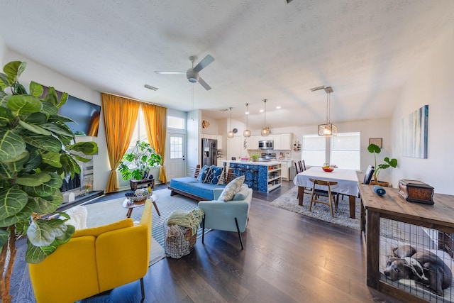 living room featuring dark wood-style floors, a textured ceiling, visible vents, and ceiling fan