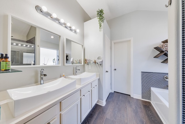 full bath featuring double vanity, vaulted ceiling, a tub to relax in, a sink, and wood finished floors