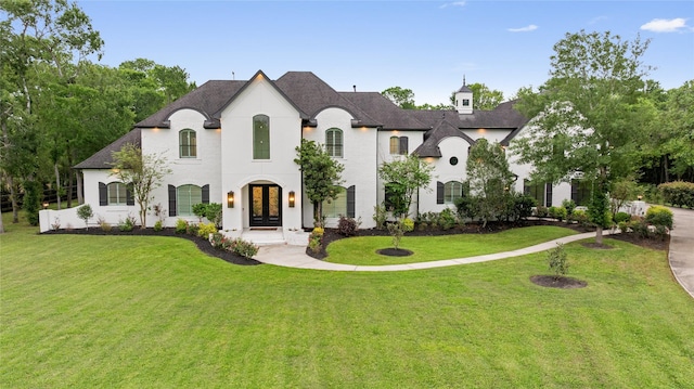 french country inspired facade with a front yard, a shingled roof, stucco siding, and french doors
