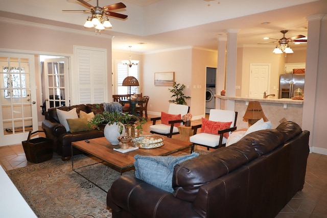 living room featuring tile patterned flooring, ceiling fan with notable chandelier, baseboards, washer / dryer, and ornamental molding