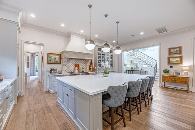 3028 Locke Ln, Houston, TX 77019 - kitchen featuring gray cabinetry, light countertops, light wood-style flooring, a large island with sink, and crown molding
