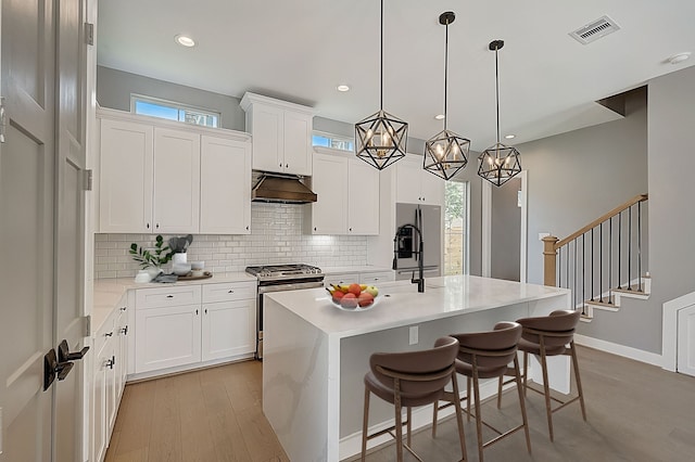 1420 Weiss St, Houston, TX 77009 - kitchen with stainless steel appliances, under cabinet range hood, light wood-style flooring, decorative backsplash, and an island with sink