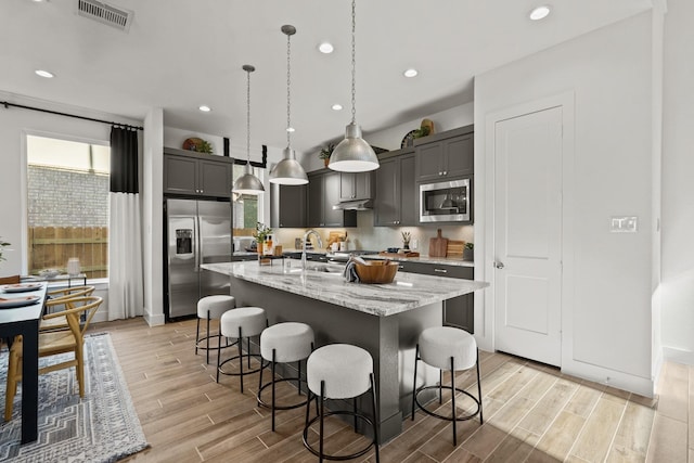 500 Dove Meadow Ln, Katy, TX 77493 - kitchen featuring appliances with stainless steel finishes, a kitchen breakfast bar, light wood-style floors, light stone counters, and pendant lighting