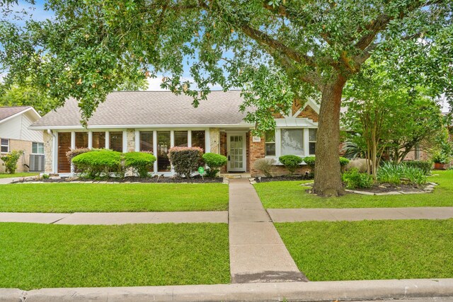 ranch-style house featuring brick siding, roof with shingles, and a front lawn