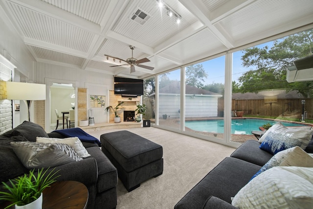 living area featuring carpet floors, a fireplace with raised hearth, a ceiling fan, beamed ceiling, and coffered ceiling