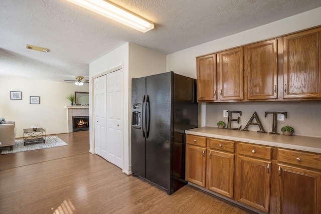 kitchen with brown cabinets, visible vents, black fridge, and a textured ceiling
