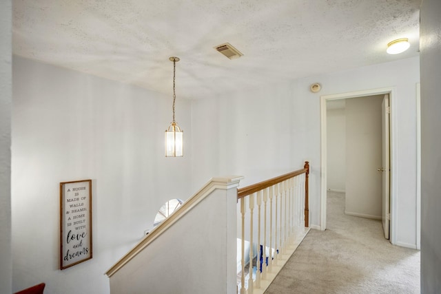 hallway with visible vents, baseboards, an upstairs landing, carpet, and a textured ceiling