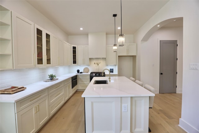 603 Neyland St, Houston, TX 77022 - kitchen featuring a sink, decorative backsplash, light wood-style flooring, arched walkways, and a kitchen island with sink