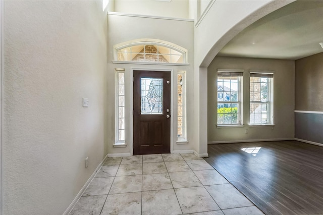 foyer entrance featuring arched walkways, light tile patterned floors, and baseboards