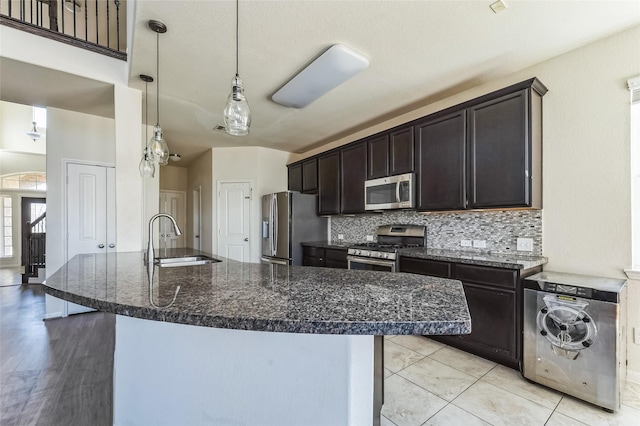 kitchen featuring tasteful backsplash, a sink, appliances with stainless steel finishes, dark brown cabinetry, and dark stone counters