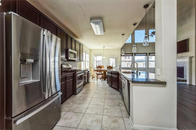 kitchen featuring dark stone countertops, a sink, hanging light fixtures, stainless steel appliances, and backsplash