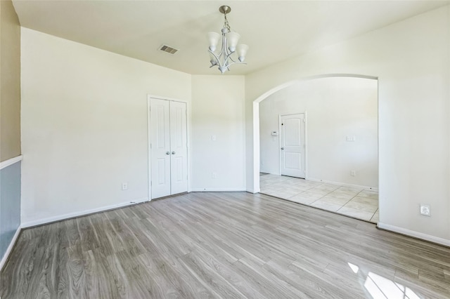 spare room featuring visible vents, baseboards, arched walkways, light wood-type flooring, and a chandelier