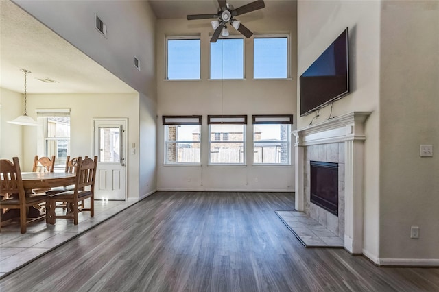 living area with a tiled fireplace, visible vents, a ceiling fan, and wood finished floors