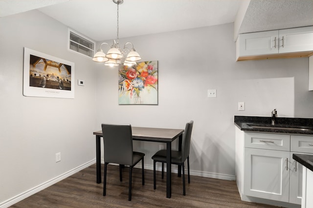 dining area with a chandelier, dark wood finished floors, wet bar, and baseboards