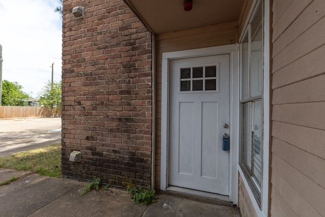 doorway to property with brick siding and fence