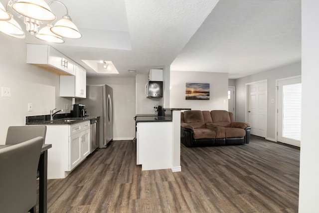 kitchen with dark wood finished floors, dark countertops, dishwasher, a sink, and open floor plan