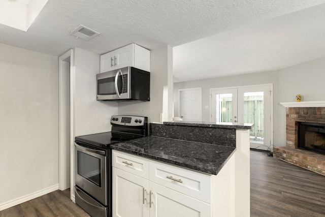 kitchen featuring dark stone countertops, appliances with stainless steel finishes, white cabinets, dark wood-style flooring, and visible vents