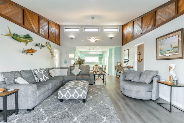 living area with a towering ceiling, ceiling fan, and wood finished floors