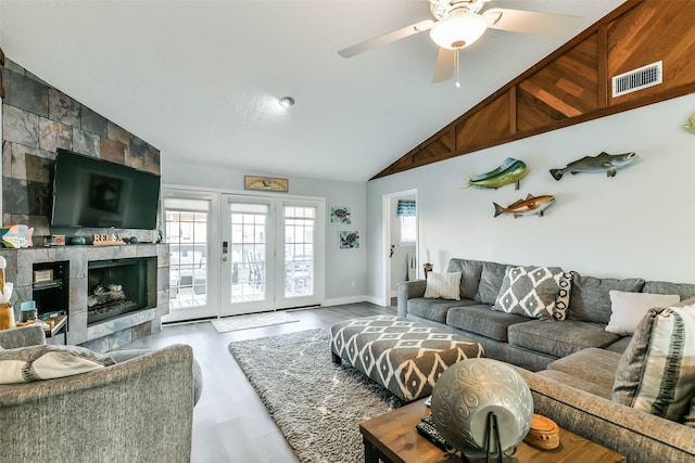 living area with ceiling fan, a fireplace, vaulted ceiling, visible vents, and wood finished floors