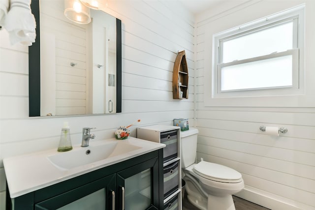 bathroom featuring wood walls, vanity, and toilet