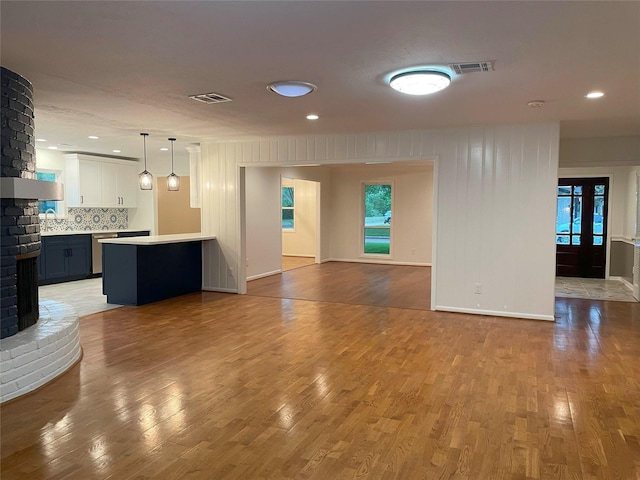 unfurnished living room featuring wood finished floors, visible vents, and a brick fireplace
