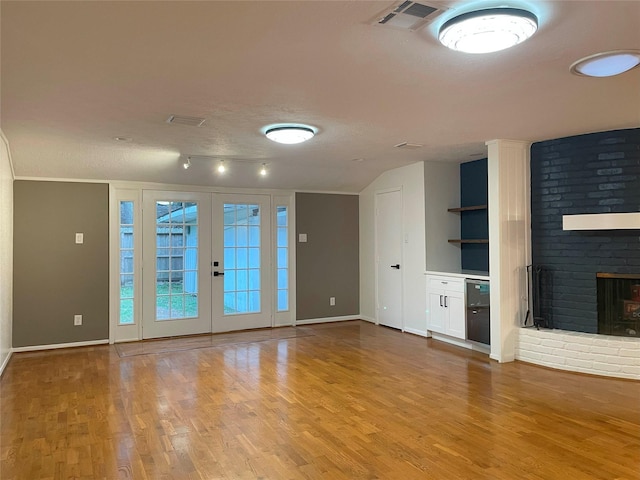 unfurnished living room with a fireplace, wood finished floors, visible vents, and baseboards
