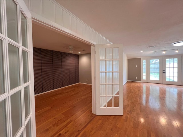 unfurnished room featuring wood finished floors, a ceiling fan, baseboards, and french doors