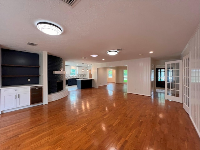 unfurnished living room featuring a textured ceiling, beverage cooler, visible vents, and light wood finished floors
