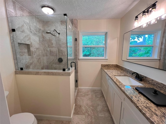 full bath with toilet, a textured ceiling, a stall shower, vanity, and baseboards