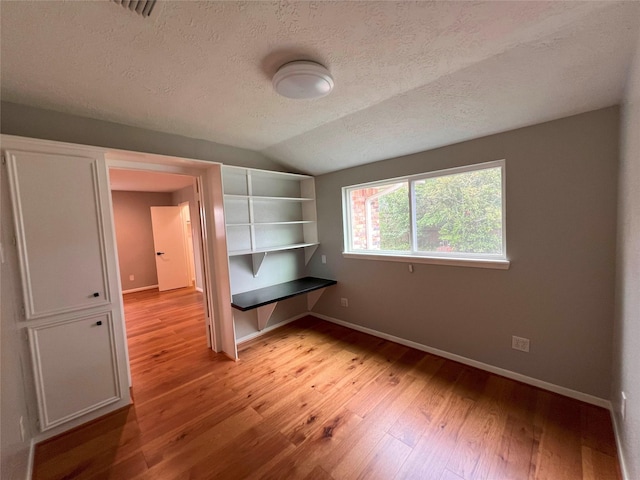 interior space with light wood-type flooring, baseboards, a textured ceiling, and lofted ceiling