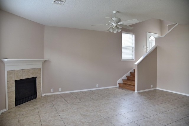 unfurnished living room with ceiling fan, light tile patterned floors, visible vents, stairway, and a tiled fireplace