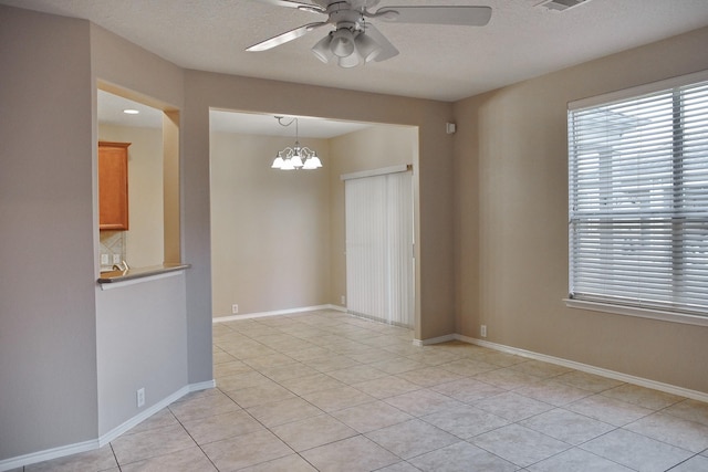 empty room with baseboards, light tile patterned floors, ceiling fan with notable chandelier, and a textured ceiling
