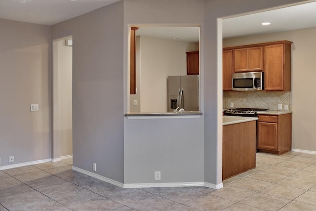 kitchen featuring light tile patterned flooring, appliances with stainless steel finishes, decorative backsplash, and brown cabinetry