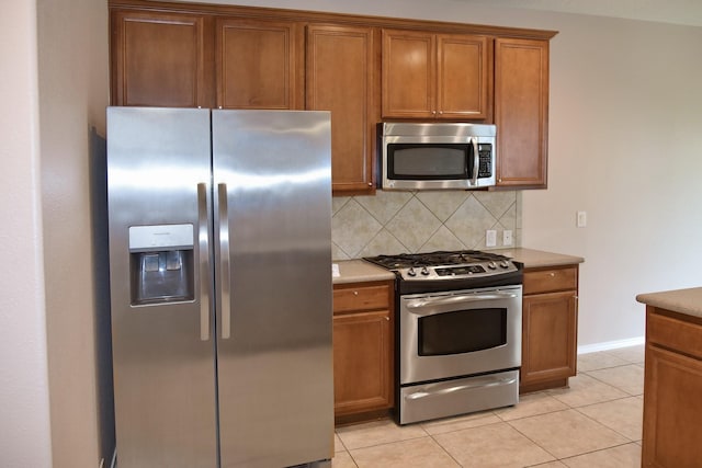 kitchen featuring brown cabinetry, tasteful backsplash, light tile patterned flooring, light countertops, and stainless steel appliances