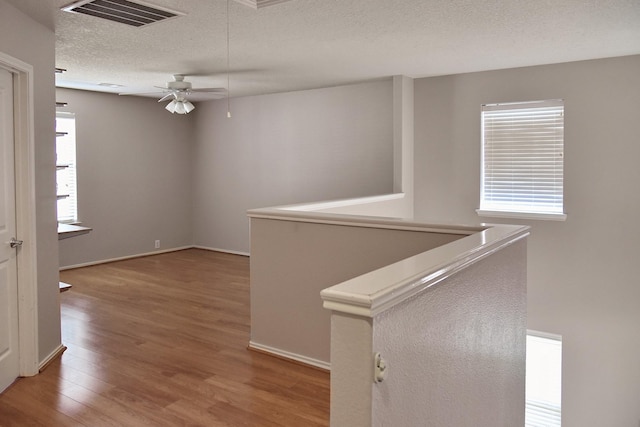 interior space featuring a textured ceiling, visible vents, wood finished floors, an upstairs landing, and baseboards