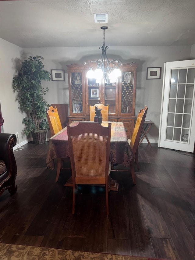dining room featuring a textured ceiling, hardwood / wood-style floors, an inviting chandelier, baseboards, and visible vents