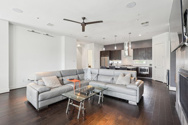 living area featuring dark wood-type flooring, visible vents, baseboards, and ceiling fan