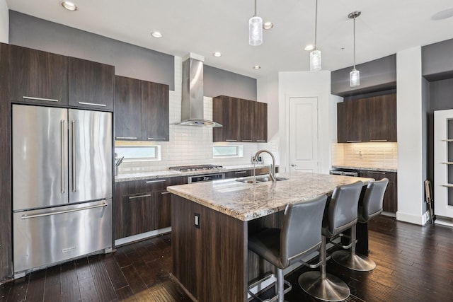 kitchen with dark brown cabinets, appliances with stainless steel finishes, wall chimney exhaust hood, and dark wood finished floors