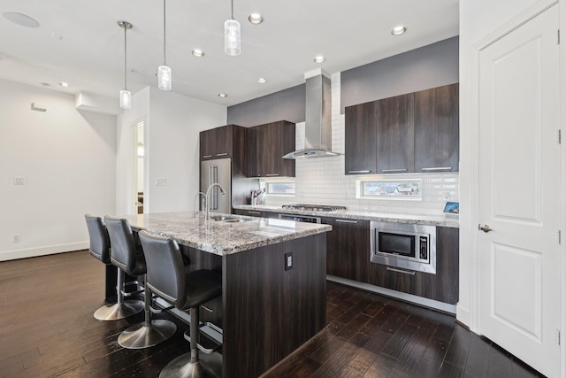 kitchen with wall chimney exhaust hood, modern cabinets, a sink, appliances with stainless steel finishes, and dark wood-type flooring