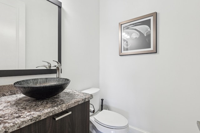 half bathroom featuring toilet, vanity, and baseboards