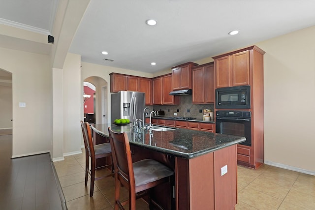 kitchen with backsplash, black appliances, under cabinet range hood, arched walkways, and a sink