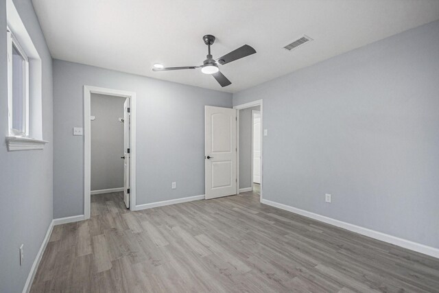 unfurnished bedroom with wood finished floors, visible vents, a walk in closet, and baseboards