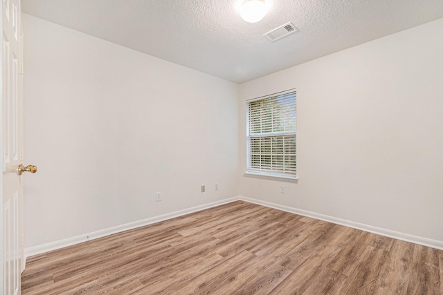 spare room with a textured ceiling, light wood-style floors, visible vents, and baseboards