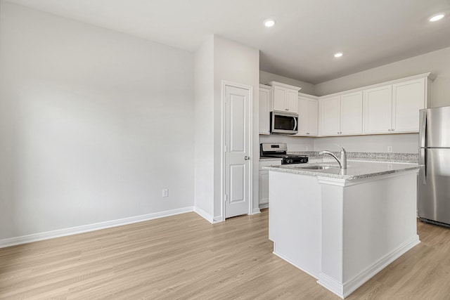 kitchen featuring light wood-style floors, white cabinets, appliances with stainless steel finishes, a kitchen island with sink, and baseboards