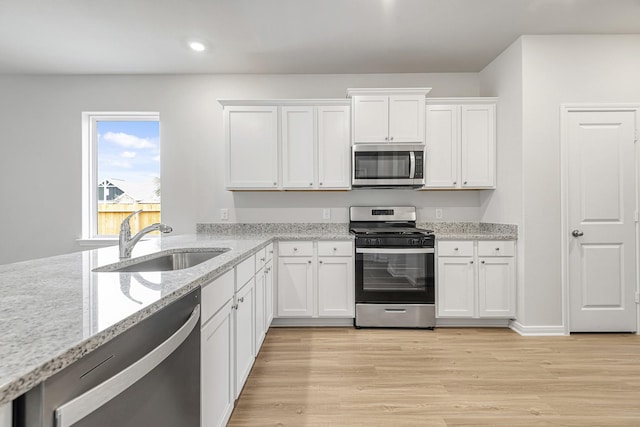 kitchen featuring light wood-type flooring, white cabinets, light stone counters, a sink, and stainless steel appliances