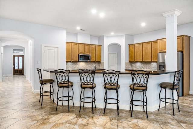 2117 Quiet Falls Ln, League City, TX 77573 - kitchen with dark countertops, a kitchen bar, brown cabinetry, and appliances with stainless steel finishes