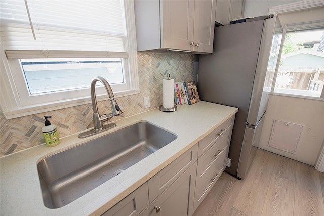 kitchen featuring light wood finished floors, a sink, freestanding refrigerator, gray cabinets, and backsplash