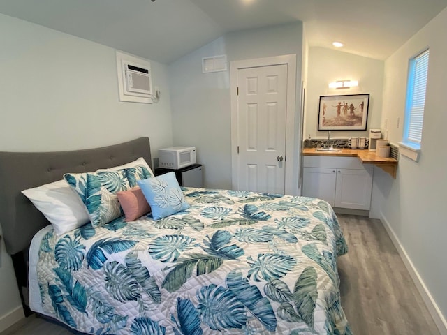 bedroom featuring light wood finished floors, ensuite bathroom, baseboards, lofted ceiling, and an AC wall unit