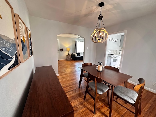 dining space featuring arched walkways, baseboards, a notable chandelier, and wood finished floors