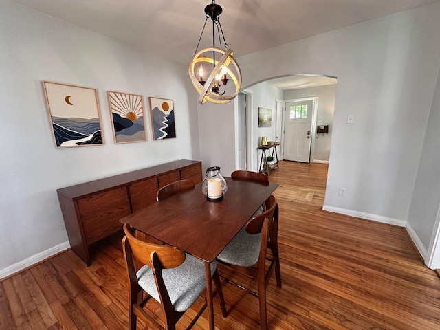 dining room featuring arched walkways, baseboards, an inviting chandelier, and wood finished floors